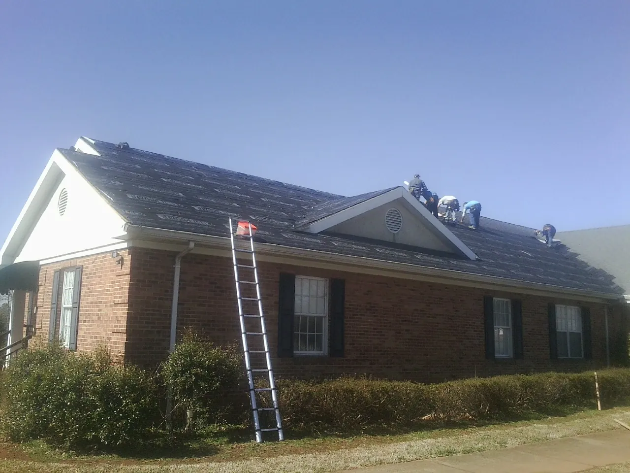 Crew tearing shingles off a brick ranch roof with a ladder set — Metal Roof Repair work by our crew in Little York