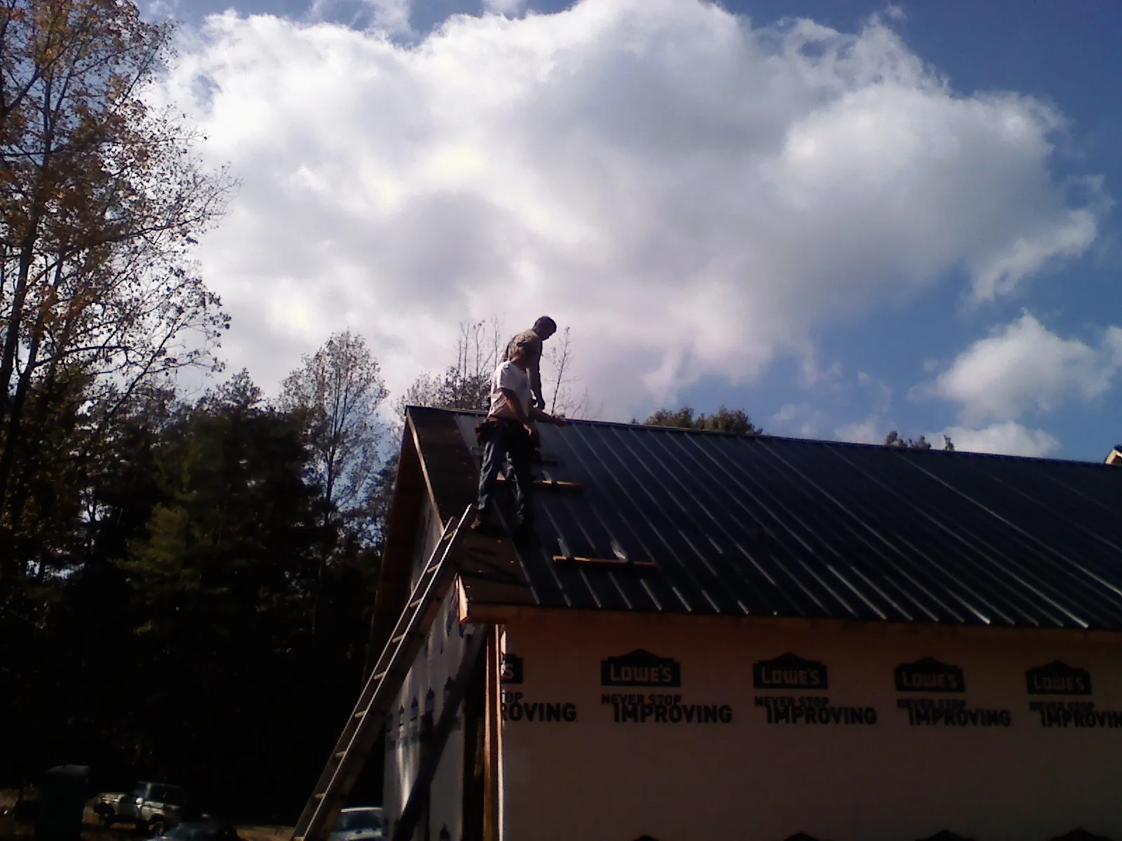 Roofer fastening dark metal panels high against a cloudy sky, from a Roof Inspection job in Little York