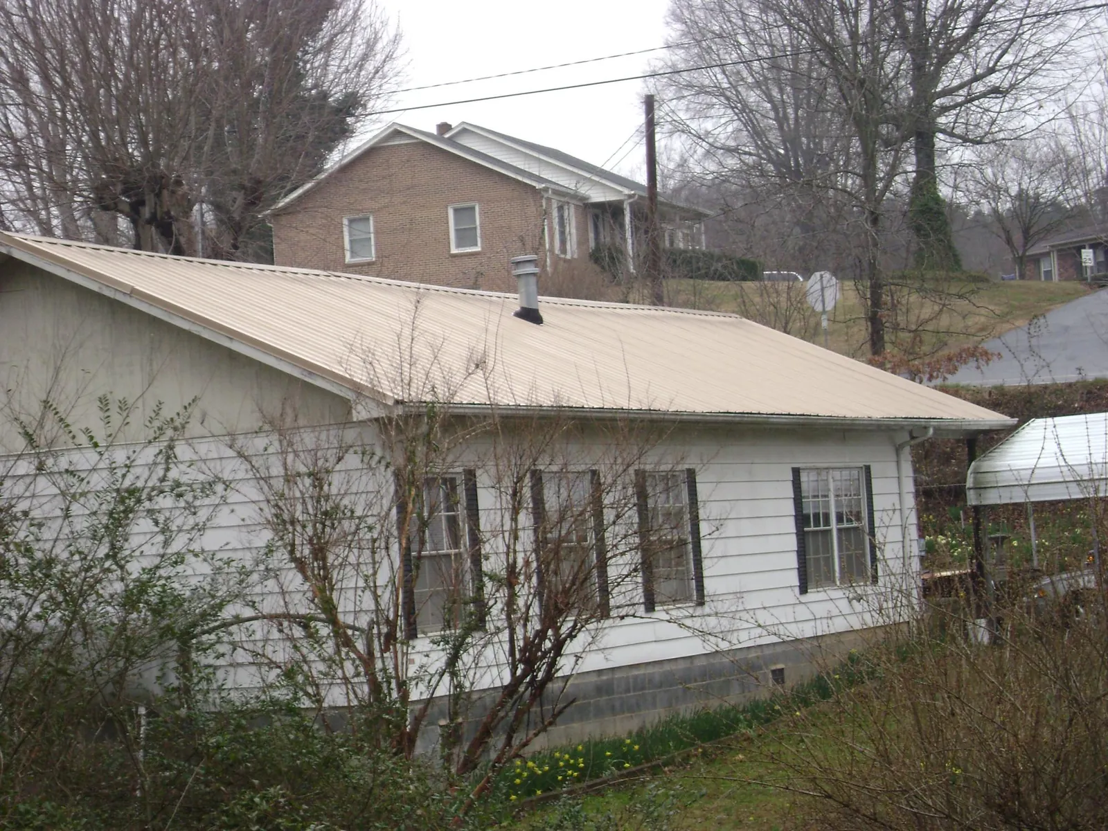 Tan metal roof on a white sided house set into a hillside — Commercial Roofing by Roofing Brothers in Little York