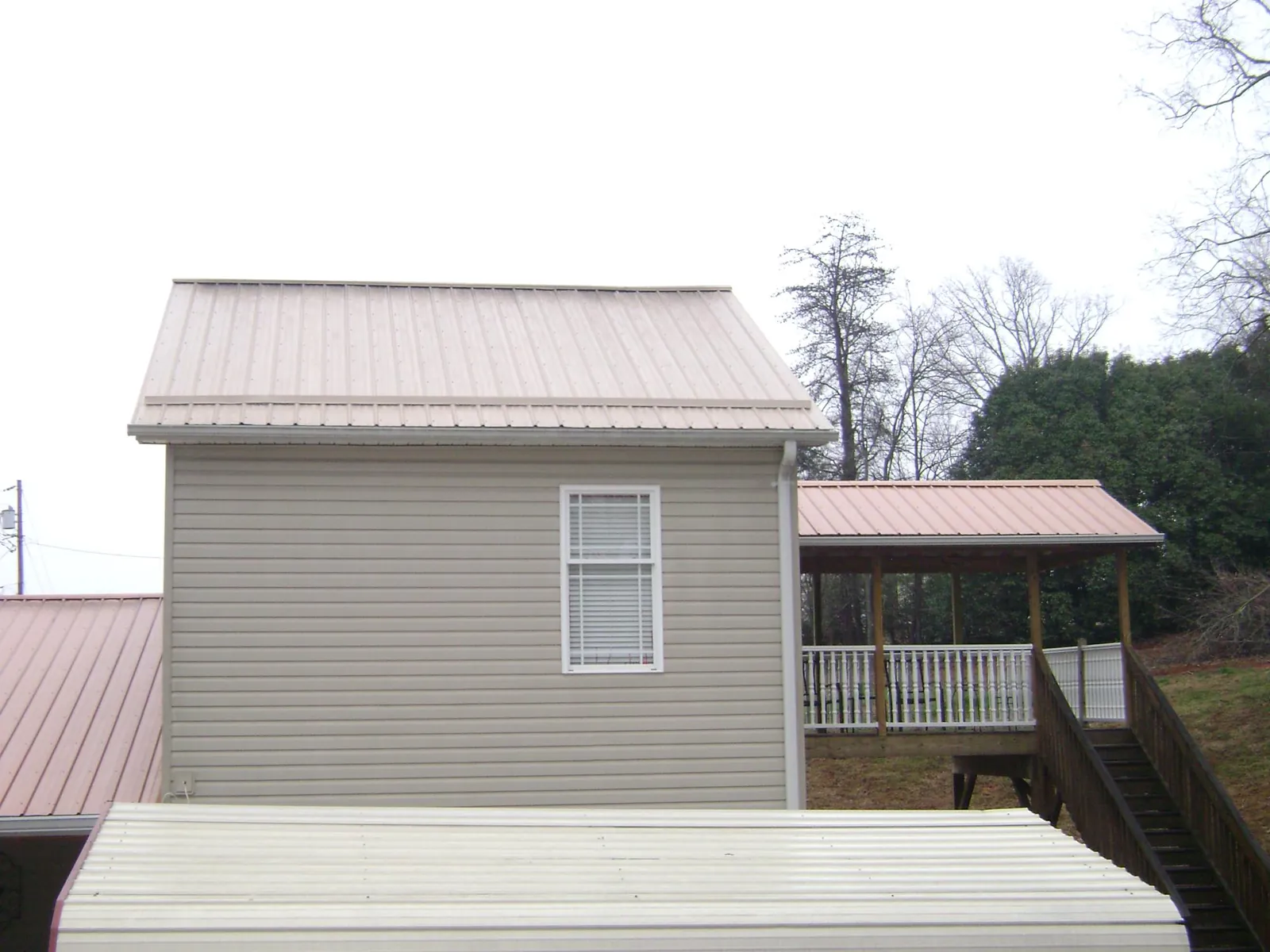 Tan metal roofs on a two story addition and attached porch, from a Roof Replacement job in Little York